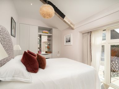 A bedroom with a bed with red pillows a wardrobe a window with curtains and a ceiling light at The Stables in Wheatley