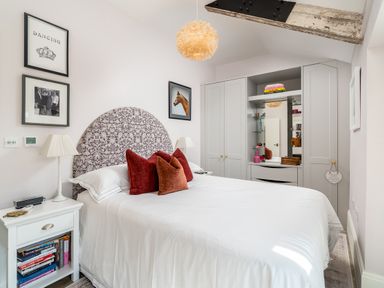 A bedroom with a bed a bedside table lamps cushion and wardrobes with a mirror at The Stables in Wheatley