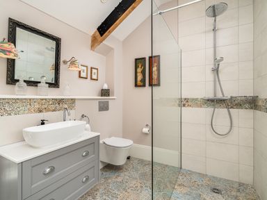 A bathroom with a shower area a floating toilet a sink on a vanity unit and artwork on walls at The Stables in Wheatley