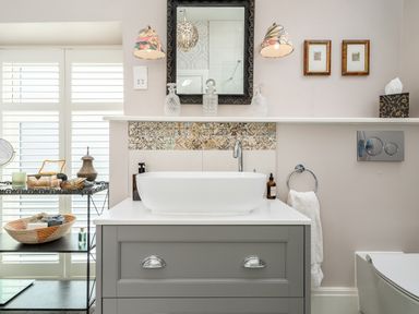 A bathroom with a white vessel sink on a gray cabinet below a mirror and two wall lamps at The Stables in Wheatley