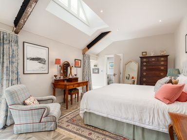 A bedroom with a bed a patterned armchair a wooden dressing table with mirror and lamps a tall dresser and a full-length mirror at The Stables in Wheatley