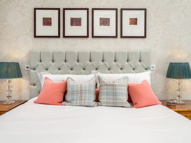 A bed with a tufted headboard and pillows between bedside tables with lamps at The Stables in Wheatley
