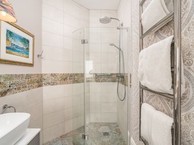 A bathroom with a walk in shower a towel rack with white towels and a painting on the wall at The Stables in Wheatley