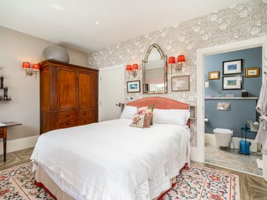A bedroom with a double bed white bed linens wooden wardrobe and an en suite bathroom at The Stables in Wheatley
