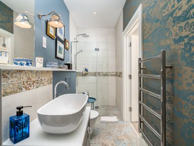 A bathroom with a white sink blue soap dispenser patterned tiles glass shower and a towel rack at The Stables in Wheatley