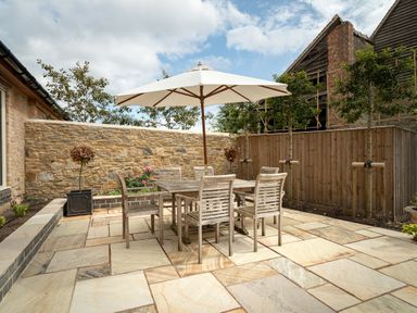 An outdoor patio with a wooden table and six chairs under a large white umbrella at The Stables in Wheatley