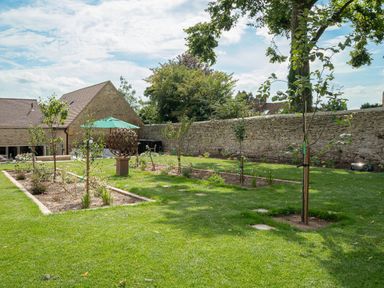 Garden with small trees and a metal sculpture near stone buildings with a green umbrella at The Stables in Wheatley
