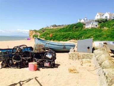 A beach with fishing nets and boats near grassy cliffs and houses at Dormouse Cottage in Burton Bradstock