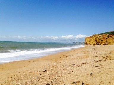 A sandy beach with sea waves and cliffs under a clear blue sky at Dormouse Cottage in Burton Bradstock