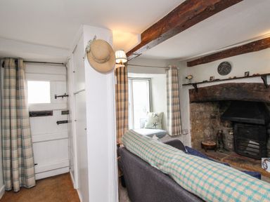 A living room with a sofa a stone fireplace wooden beams and plaid curtains at Dormouse Cottage in Burton Bradstock