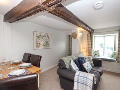 A living room with a dining table set for four a gray sofa with cushions and a window seat at Dormouse Cottage in Burton Bradstock