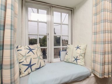 A window seat with starfish patterned cushions and checkered curtains at Dormouse Cottage in Burton Bradstock