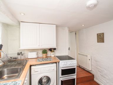 A kitchen with a sink washing machine stove wooden countertops white cabinets and a heater on the wall at Dormouse Cottage in Burton Bradstock