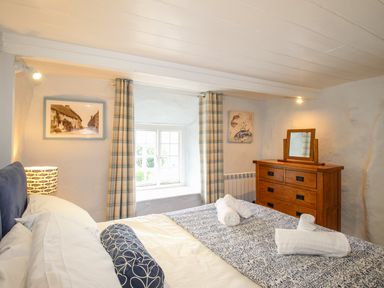 A bedroom with a bed a wooden dresser a window with curtains and framed pictures at Dormouse Cottage in Burton Bradstock