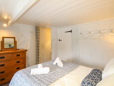 A bedroom with a patterned bedspread white rolled towels wooden dresser with mirror and wall-mounted hangers at Dormouse Cottage Burton Bradstock