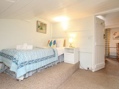 A bedroom with a single bed with patterned bedding a white nightstand and a lamp at Dormouse Cottage in Burton Bradstock