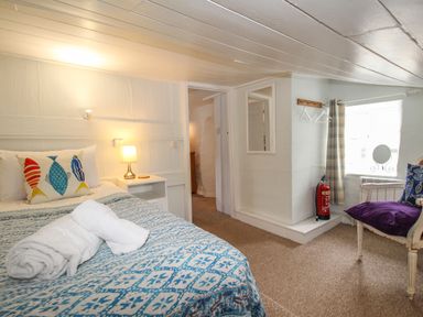 A bedroom with a bed with fish cushions and a blue patterned blanket next to a bedside table with a lamp at Dormouse Cottage in Burton Bradstock