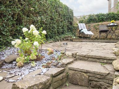 A stone patio garden with white flowers and patio furniture at Dormouse Cottage in Burton Bradstock