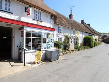A street view of thatched roof cottages with a farm shop and post office at Dormouse Cottage in Burton Bradstock