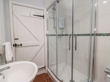 A bathroom with a white sink a towel rail with white towel a glass shower enclosure and a white wooden door with black hardware at Dormouse Cottage in Burton Bradstock