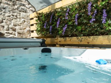 A hot tub in an outdoor area with a stone wall and plants at Wonderland in Tweedmouth, Berwick-Upon-Tweed