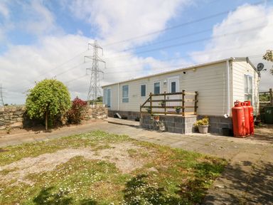An exterior view of a small house with a paved patio area and grass with flowers at Gwel Y Mor Nasareth near Caernarfon