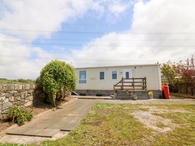 A mobile home with a small wooden deck and potted plants in a garden with paved walkway and stone wall at Gwel Y Mor in Nasareth near Caernarfon