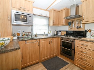 A kitchen with wooden cabinets a microwave an oven a gas hob a sink and various kitchen utensils at Gwel Y Mor in Nasareth near Caernarfon