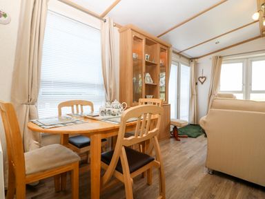 A dining area with a wooden table and chairs next to a china cabinet and beige sofas in a room at Gwel Y Mor Nasareth near Caernarfon