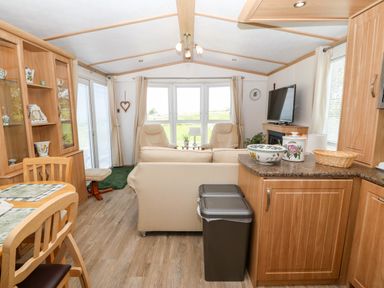 A living room and kitchen area with dining table chairs sofa armchairs television and kitchen cabinets at Gwel Y Mor in Nasareth near Caernarfon