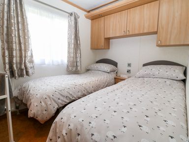 A bedroom with two single beds with sheep patterned bedding and wood cupboards above at Gwel Y Mor in Nasareth near Caernarfon