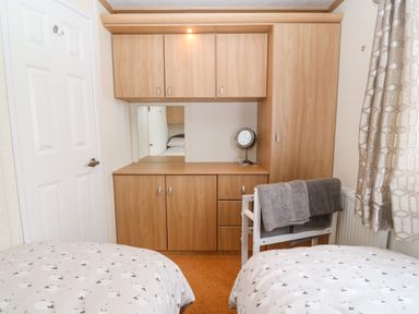 A bedroom with two beds a wooden wardrobe with cabinets a small mirror and a chair with towels at Gwel Y Mor in Nasareth near Caernarfon