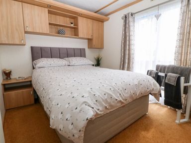 A bedroom with a double bed with sheep patterned bedding and overhead wooden cabinets at Gwel Y Mor in Nasareth near Caernarfon