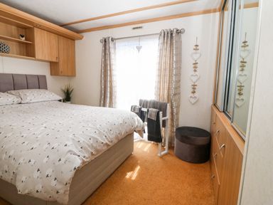 A bedroom with a bed a window with curtains a towel rack a round ottoman and a wardrobe with mirrored doors at Gwel Y Mor Nasareth near Caernarfon