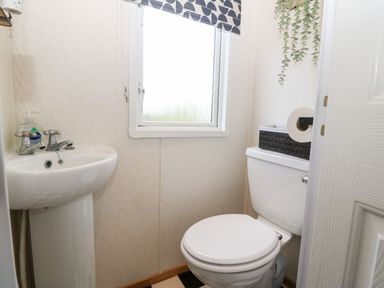 A small bathroom with a toilet sink window and a black basket above the toilet at Gwel Y Mor in Nasareth near Caernarfon