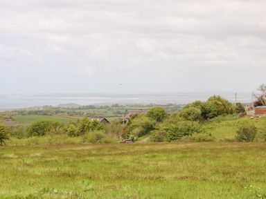 A landscape view of green fields trees and houses with a distant view of the sea and sky at Gwel Y Mor in Nasareth near Caernarfon
