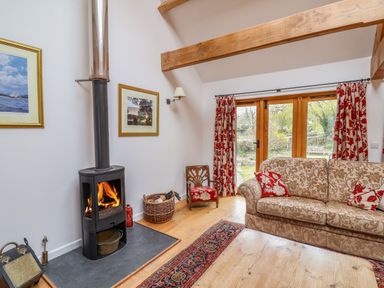 A living room with a wood stove a sofa with patterned cushions and wooden beams at Bridge Cottage in Dalwood