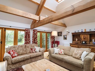 A living room with two patterned sofas wooden beams and large windows at Bridge Cottage in Dalwood