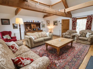 A living room with patterned sofas a wooden coffee table and exposed ceiling beams at Bridge Cottage in Dalwood