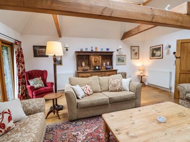 A living room with sofas a wooden coffee table a red armchair and a wooden cabinet at Bridge Cottage in Dalwood
