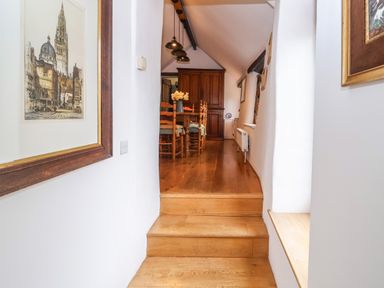 A hallway with wooden steps leading up to a dining area with a wooden table and chairs and a wooden cabinet at Bridge Cottage in Dalwood