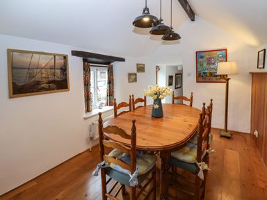 A dining room with a wooden table and chairs a vase with flowers and framed pictures on walls at Bridge Cottage in Dalwood