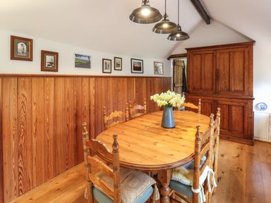 A dining room with a wooden table and chairs with flowers in a vase and a large wooden cabinet at Bridge Cottage in Dalwood