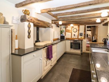 A kitchen with wooden beams white cabinets a stove microwave and a sink at Bridge Cottage in Dalwood