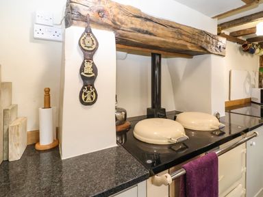 A kitchen counter with a paper towel holder and a stove with two cream covers under a wooden beam at Bridge Cottage in Dalwood