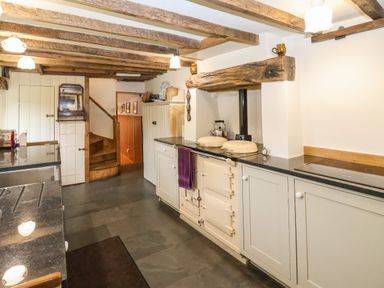 A kitchen with wooden ceiling beams a cream stove cabinets and a wooden staircase at Bridge Cottage in Dalwood