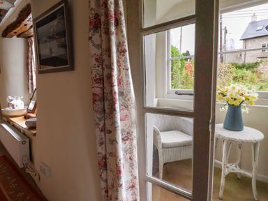 A wicker chair and a small round table with a vase of flowers by a window at Bridge Cottage in Dalwood