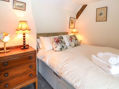 A bedroom with a bed white bedding floral pillows a wooden chest of drawers and two lit lamps at Bridge Cottage in Dalwood