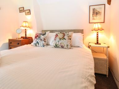 A bedroom with a double bed two floral pillows two bedside tables with lamps and framed pictures on the walls at Bridge Cottage in Dalwood