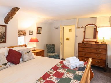 A bedroom with a wooden bed a dresser with a mirror a bedside table with a lamp and a chair at Bridge Cottage in Dalwood